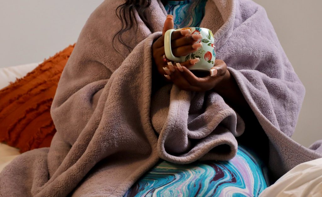 person wrapped in a blanket and drinking from a mug